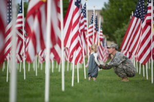 Image of young girl with her dad in military uniform running through field filled with US flags.