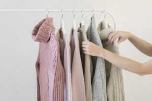 Image of a woman's arms selecting from pastel colored sweaters on a clothes rack.